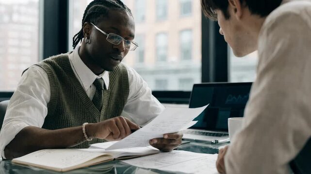 Medium shot of a financial advisor aligning personal loan proposals with a clients debt relief plan with outoffocus digital charts on a laptop screen in the background.