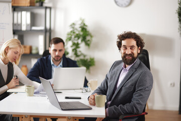 Obraz premium Business team meets in bright office space to brainstorm ideas. Team members use laptops and discuss work while enjoying drinks. Productive atmosphere supports teamwork and success.