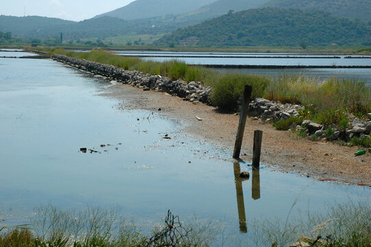 Two wooden posts reflect in the shallow water of ancient stone salt pans under green hills in the town of Ston