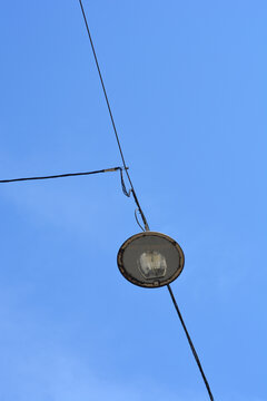 A low angle shot of a circular street lamp suspended from a catenary overhead wire system against a clear blue sky