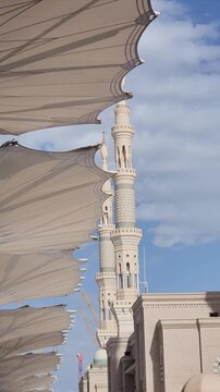 Ornately designed large umbrellas at Al-Masjid an-Nabawi, Medina, Saudi Arabia, feature geometric patterns. Made from durable fabric, they provide shelter and shade. The umbrellas are mounted on tall,