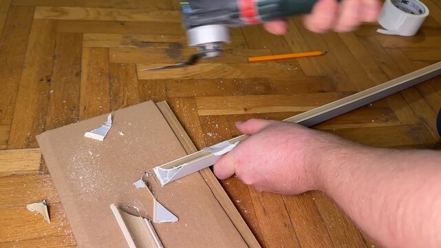 Close up of hands cutting cardboard on wooden parquet floor, using oscillating multitool for DIY renovation, gritty workshop mood, home improvement and repair concept