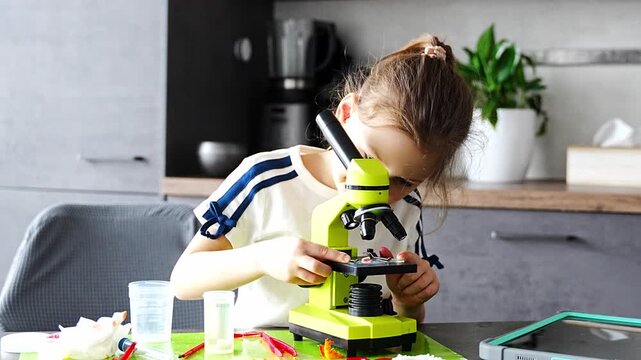 Young girl placing small grown crystal onto microscope slide during home science experiment. Detailed scientific observation and hands on STEM learning through crystal analysis.