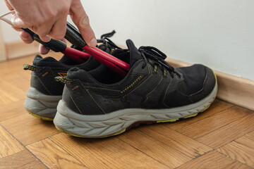 Closeup photo of man drying his sneakers with electric shoe dryer. Electric shoe dryer inserted into wet running sneakers on wooden floor
