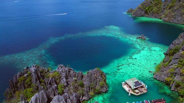 Tropical island landscape featuring jagged limestone karsts rising from deep blue and emerald green lagoons with boats and swimmers. Magic aerial view drone shot panorama from above