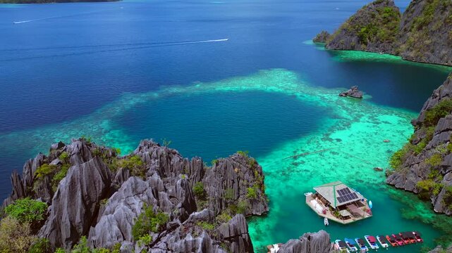 Tropical island landscape featuring jagged limestone karsts rising from deep blue and emerald green lagoons with boats and swimmers. Amazing aerial view descending panorama drone