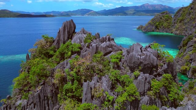 Tropical island landscape featuring jagged limestone karsts rising from deep blue and emerald green lagoons with boats and swimmers. Smooth aerial view fly reverse panorama drone