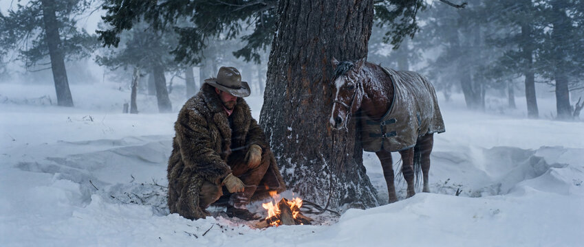 A cowboy and horse take shelter from a storm near a large tree in the forest. Illustration on the theme of lifestyle and cinema.