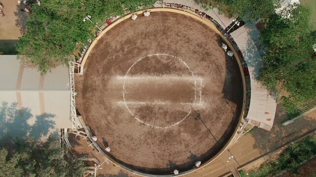 Circular arena used for scaramuza equestrian contest surrounded by trees and small structures in Colima, Mexico. Ascending aerial top down view.