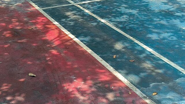 Dance of shadows: Flickering sunlight patterns on a weathered crimson court, echoing the silence of an empty arena
