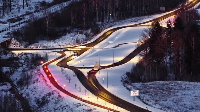 Winter roads merging, vehicles traveling through snowy interchange at dusk