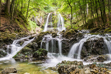 Fototapeta premium Scenic waterfall in lush green forest with rocky riverbed in summer morning in Bavaria Germany 