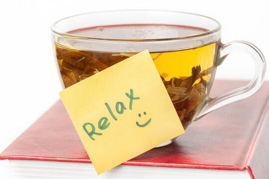 Book with a glass cup of herbal tea on top of it and yellow sticker note Relax isolated white background macro
