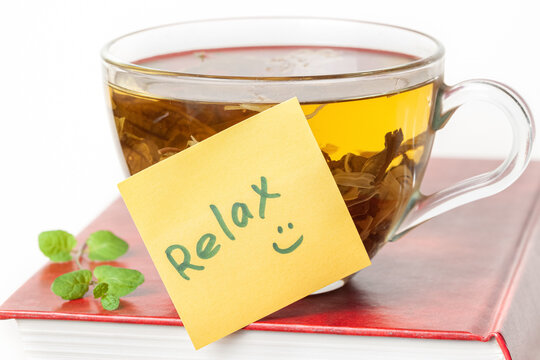 Book with a glass cup of herbal tea on top of it and yellow sticker note Relax isolated white background macro