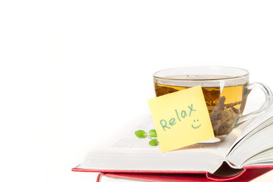 Stack of books and one opened book on top with yellow sticker note Relax and a glass cup of herbal tea front view isolated white background space for text copy space macro