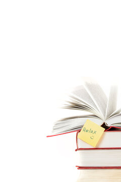 Stack of books and one opened book on top with yellow sticker note Relax front view isolated white background space for text copy space vertical macro
