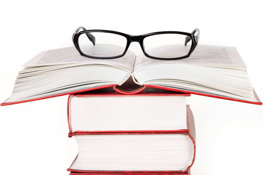 Stack of books one opened book with glasses on top front view isolated white background macro
