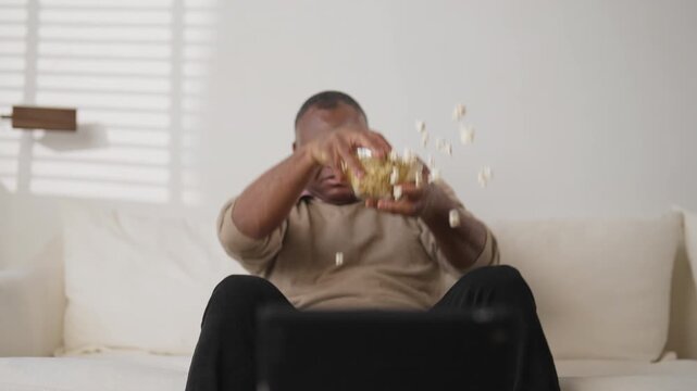 TV viewer relaxing in front of television set and eating popcorn in weekend. Mature african american man spending evening at home, enjoying favorite series or sport match, entertainment and leisure