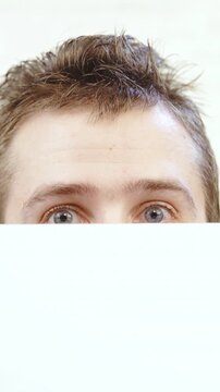 Male person peeking tom look over a white wall close-up on eyes