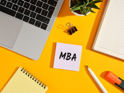 Mba written on sticky note on student desk with laptop and notebook