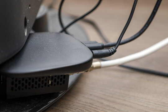 A black multimedia box is connected to a TV using various cables on a wooden surface. The compact media player provides access to streaming services and digital content,