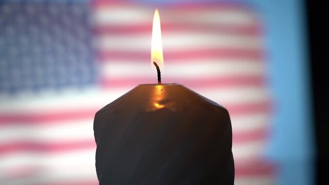 The candle flame glows against the blurred background of the US flag. Mourning in the United States of America for the dead. High quality FullHD footage