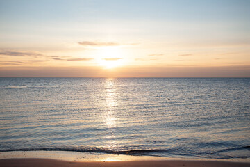 Obraz premium Beautiful landscape of a tranquil sea at sunrise. Soft pastel colors of the sky reflect on the water surface with gentle ripples on the sand. Serene morning atmosphere at the coastline.