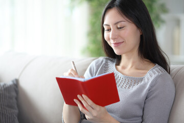 Satiesfied asian woman writing notes in red agenda
