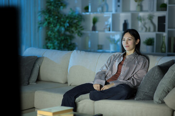 Serious asian woman watching tv at home in the night