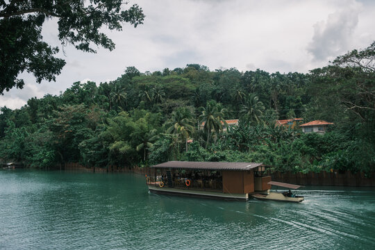 Floating restaurant boat navigating the lush tropical Loboc River on Bohol Island, Philippines. Scenic jungle cruise showcasing dense green vegetation and Southeast Asian ecotourism