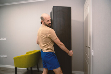 Fototapeta premium Man Moving Tall Dark Wardrobe Cabinet During Home Renovation or Relocation