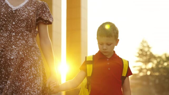 Boy with backpack walking to school at sunrise, Mother and son holding hands on the first day of school, Happy child ready for a new school year, Little boy in red shirt going to class in the morning
