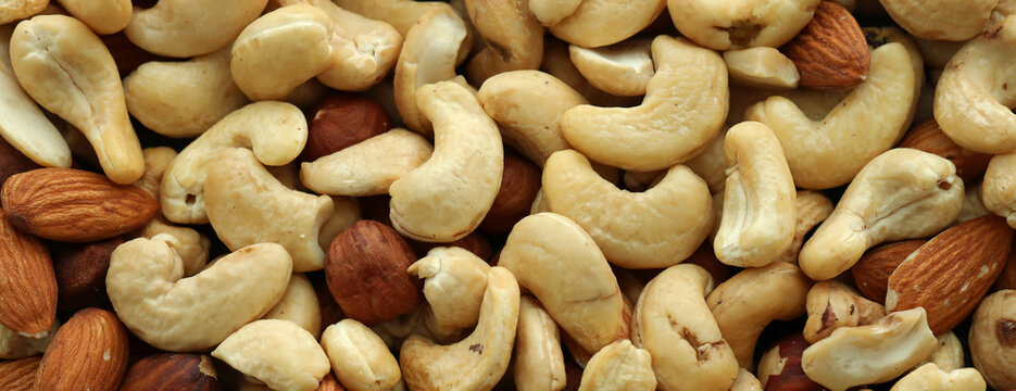 Almond and cashew nuts in big pile on table close up. Large amount of brown nuts
