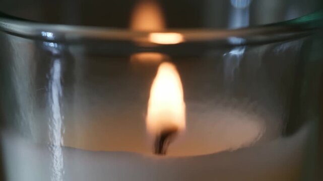 An ultra slow motion shot of a candle flame flickering in a glass jar, with light dancing on its textured surface for creating intimate, atmospheric moods