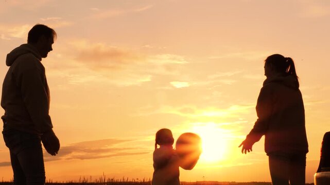 Family playing with ball near car at sunset, silhouettes. Father, mother, daughter throwing ball in circle, laughing, having fun joyful good time in field, creating pleasant unforgettable memories.