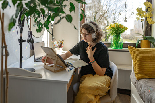 Young person studying creatively at desk with headphones in cozy bedroom
