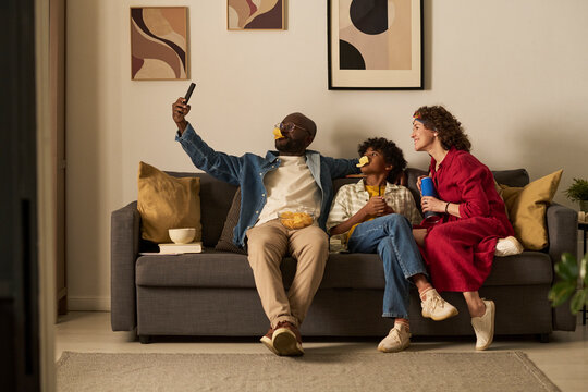 Family taking selfie on couch at home with chips and snacks