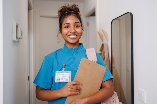 Nurse assistant smiling indoors with clipboard at home visit