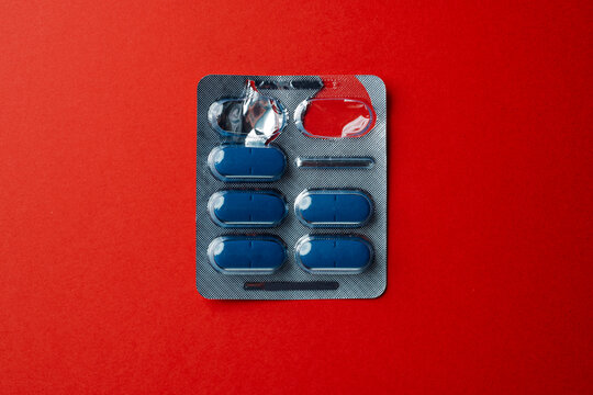 Partially used medicine blister with dark blue tablets on red background