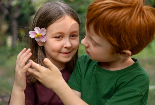 Girl and boy in garden looking at flower in her hair