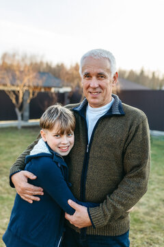 Grandfather and grandson smiling and embracing outdoors in backyard