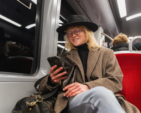 Smiling commuter browsing smartphone on urban metro in stylish outfit