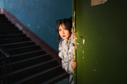 Woman in fur coat peering through doorway in old entrance with blue wall