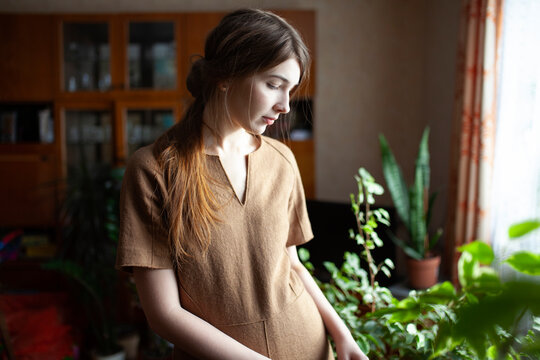 Woman in brown dress looking at houseplants indoors in vintage home