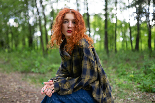 Red haired woman in plaid shirt sitting in forest in summer