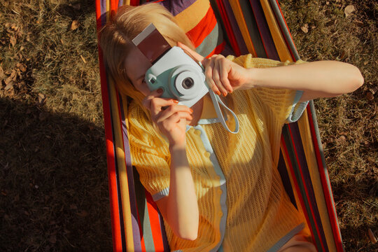 Woman taking photo while lying in striped hammock outdoors in spring