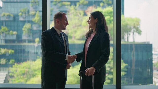 Business Deal: Professional colleagues, sealed with a handshake, forge a partnership amidst the vibrant greenery visible through a panoramic window.