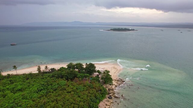 Aerial drone footage of Oar paradise small island, with Sumur city horizon, in Pandeglang regency, Java island, Indonesia, nearby Ujung Kulon national park, in stormy weather, Umang island behind