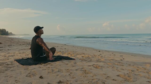 Man sitting on a tropical beach performing upward salute prayer yoga pose with calm waves and blue skies, capturing mindfulness, relaxation, and peaceful coastal living.