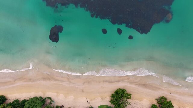 Overhead view of Magura Beach shows turquoise shallow water with dark reef patches and a pale sand shoreline bordered by tropical trees